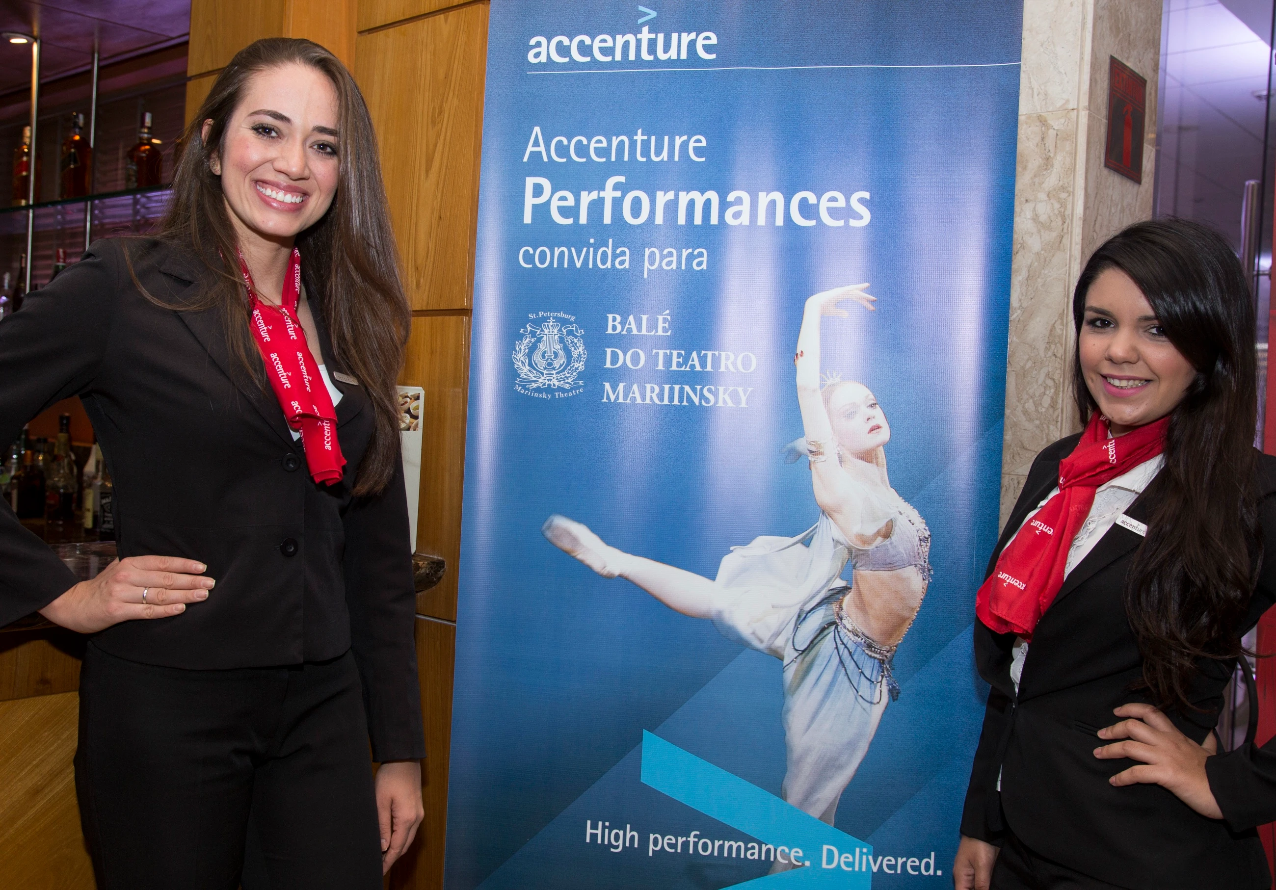 Recepcionistas ao lado do banner da Accenture com a campanha do Balé do Teatro Mariinsky.