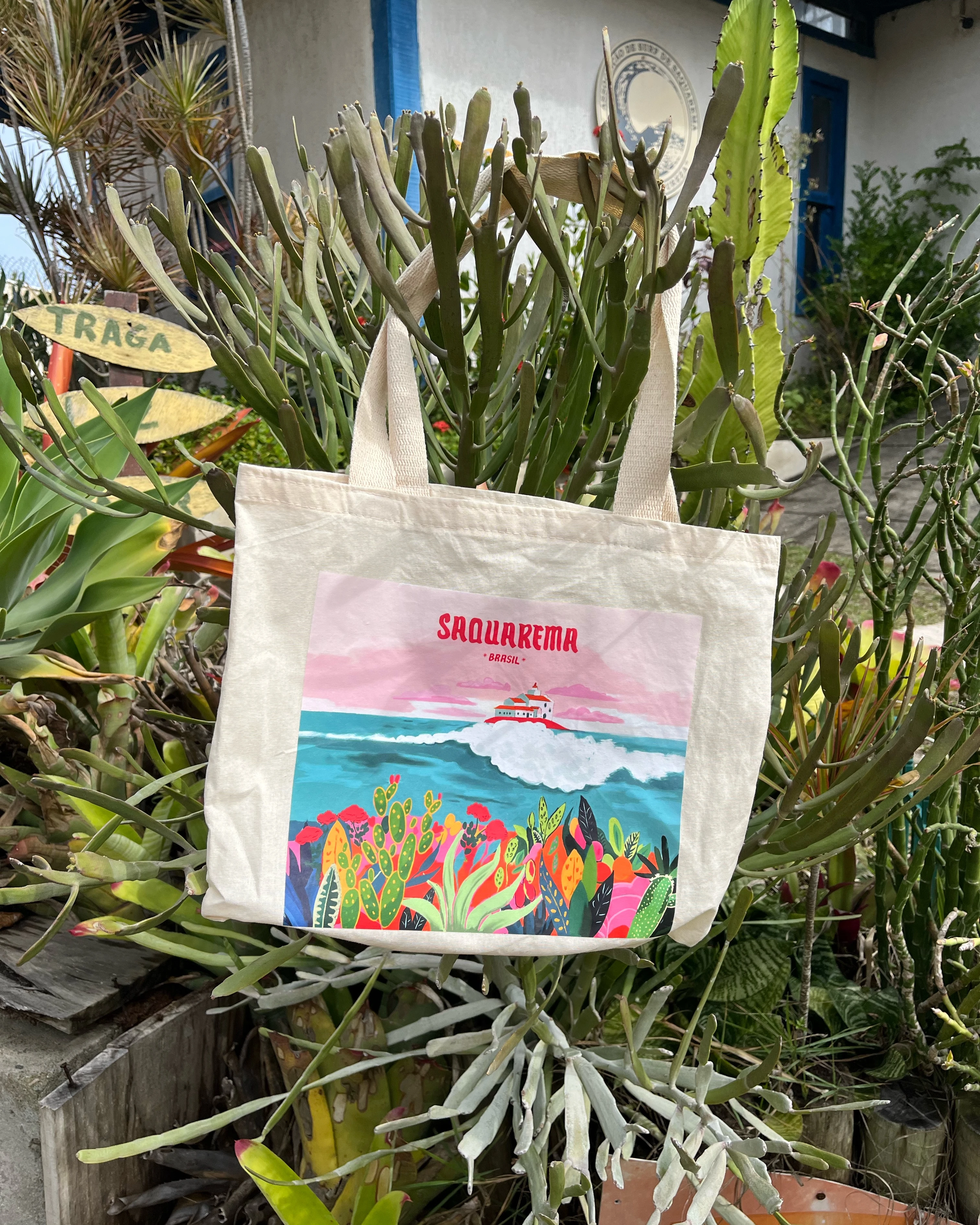 Ecobag com a ilustração da praia de Saquarema pendurada entre plantas.