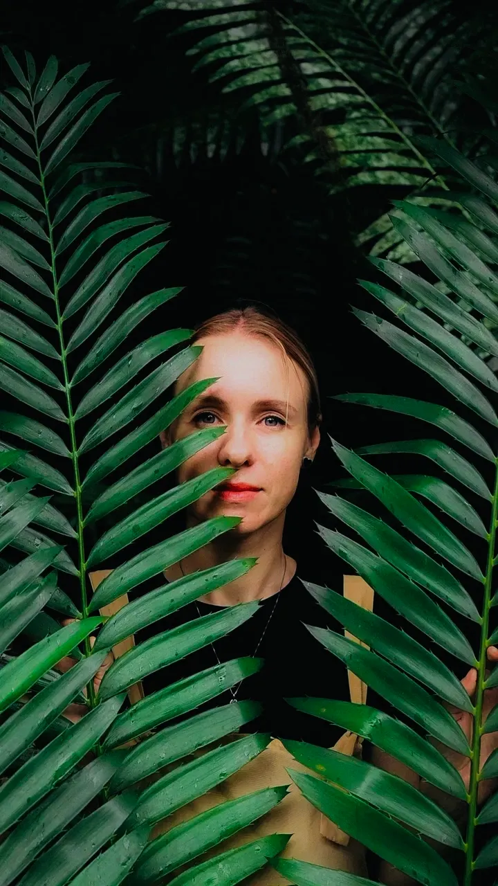 Retrato de Janna Brilyantova entre folhas grandes de samambaia, olhando para a câmera.
